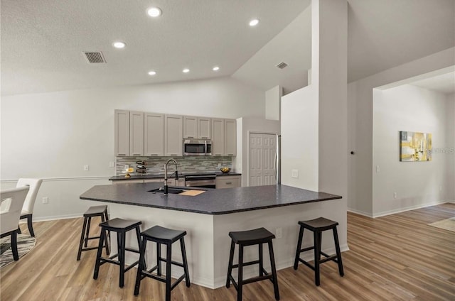 kitchen featuring gray cabinetry, stainless steel appliances, sink, light hardwood / wood-style floors, and a breakfast bar