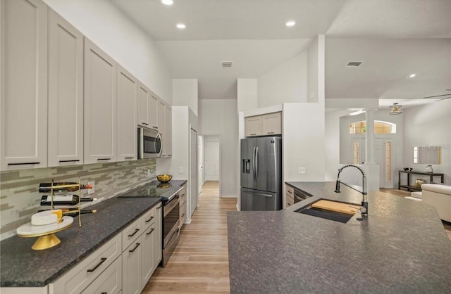 kitchen with stainless steel appliances, sink, backsplash, high vaulted ceiling, and light hardwood / wood-style flooring