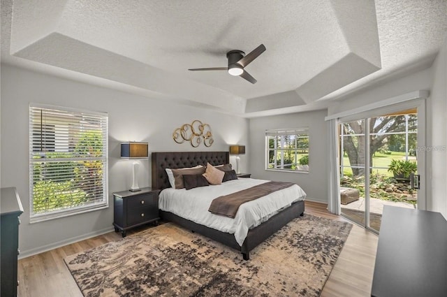 bedroom with access to outside, light hardwood / wood-style floors, ceiling fan, and a tray ceiling