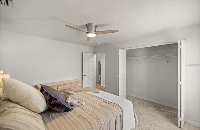 bedroom with a closet, a textured ceiling, light colored carpet, and ceiling fan