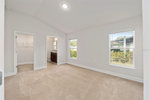 unfurnished bedroom featuring a spacious closet, connected bathroom, lofted ceiling, and light colored carpet