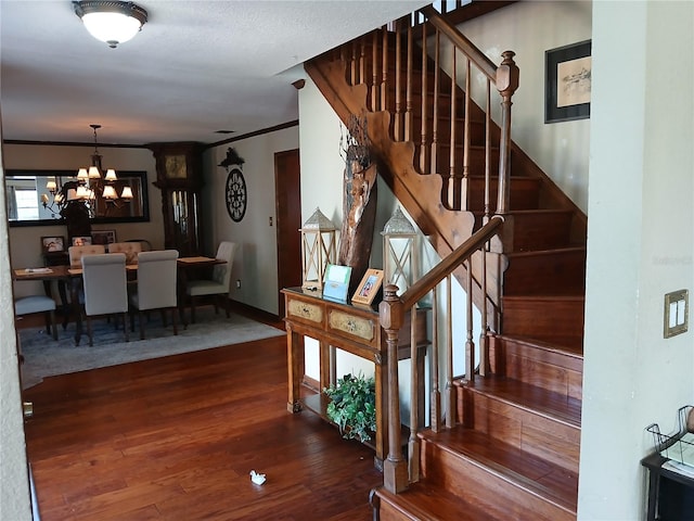 staircase with hardwood / wood-style floors, ornamental molding, and a notable chandelier