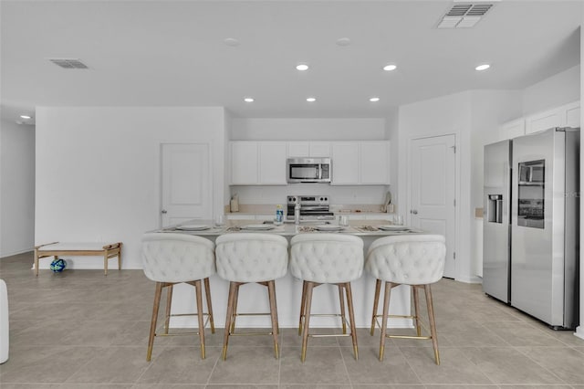 kitchen featuring appliances with stainless steel finishes, a breakfast bar, white cabinetry, and an island with sink