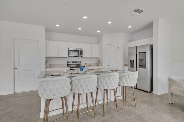 kitchen featuring a kitchen breakfast bar, white cabinetry, stainless steel appliances, and a center island with sink