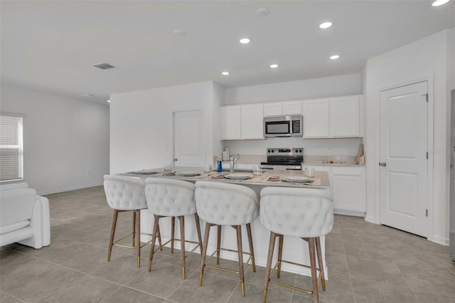 kitchen featuring a kitchen island with sink, white cabinets, a kitchen bar, and stainless steel appliances