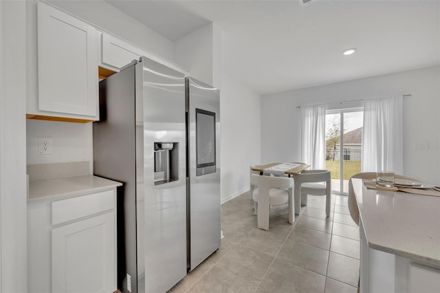 kitchen featuring white cabinetry, stainless steel fridge, light tile patterned flooring, and light stone counters