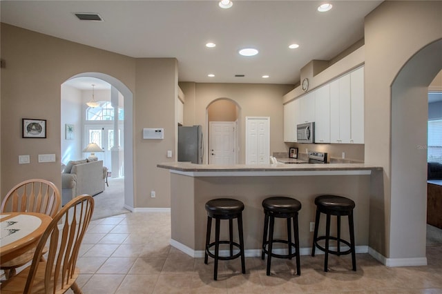 kitchen with kitchen peninsula, white cabinetry, stainless steel appliances, and a kitchen bar