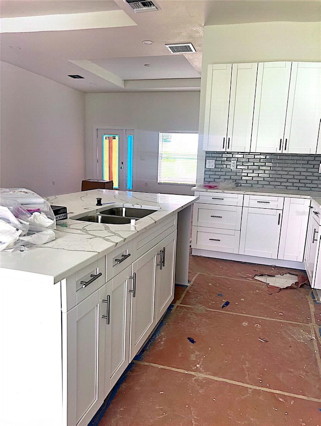 kitchen featuring a kitchen island, sink, light stone countertops, white cabinetry, and tasteful backsplash