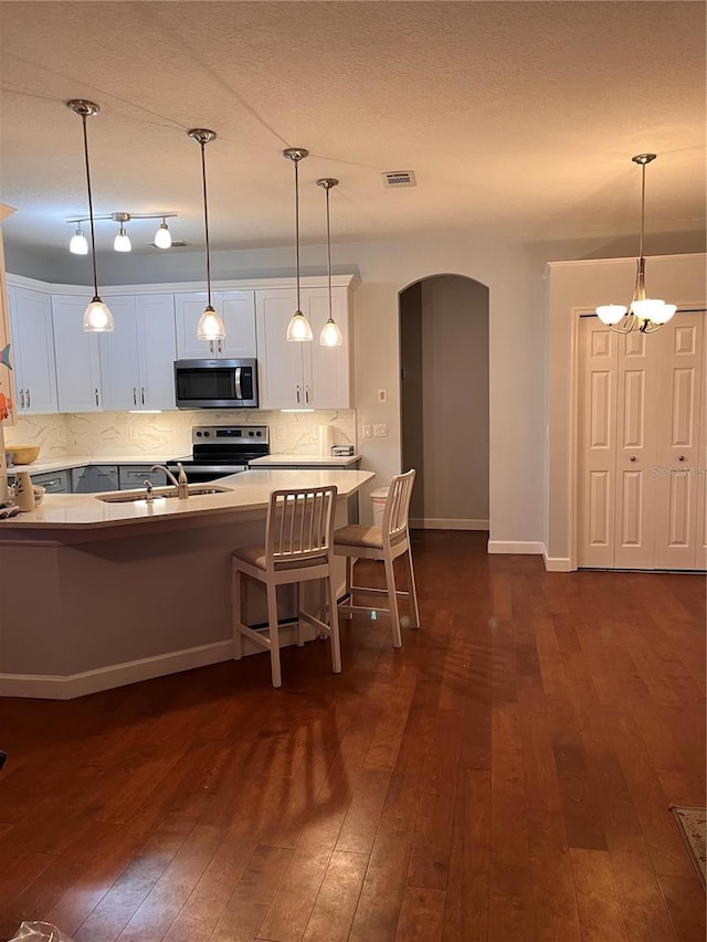 kitchen with decorative backsplash, stainless steel appliances, white cabinets, dark hardwood / wood-style floors, and hanging light fixtures