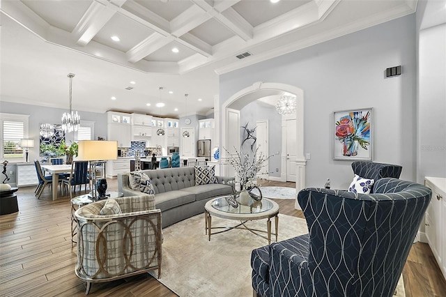 living room with coffered ceiling, beam ceiling, a notable chandelier, ornamental molding, and light hardwood / wood-style flooring