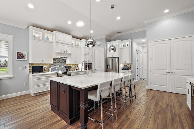 kitchen with appliances with stainless steel finishes, an island with sink, decorative light fixtures, white cabinets, and dark wood-type flooring