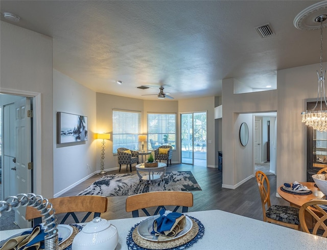 living room with a textured ceiling, ceiling fan with notable chandelier, and dark wood-type flooring