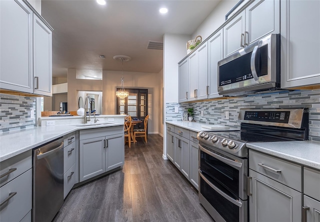 kitchen with decorative backsplash, dark hardwood / wood-style flooring, stainless steel appliances, sink, and decorative light fixtures