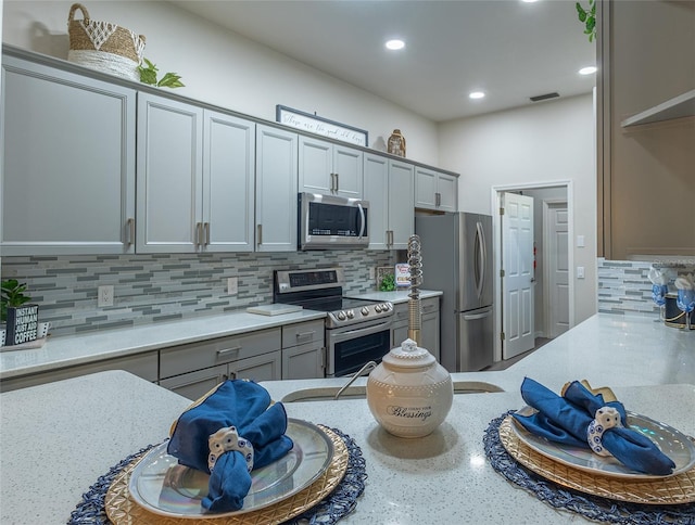 kitchen featuring backsplash, gray cabinets, light stone counters, and stainless steel appliances