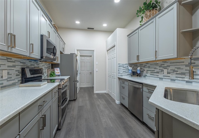 kitchen featuring stainless steel appliances, light stone counters, backsplash, wood-type flooring, and gray cabinets