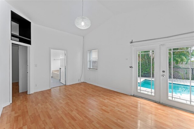 unfurnished bedroom featuring french doors, access to exterior, high vaulted ceiling, and light wood-type flooring