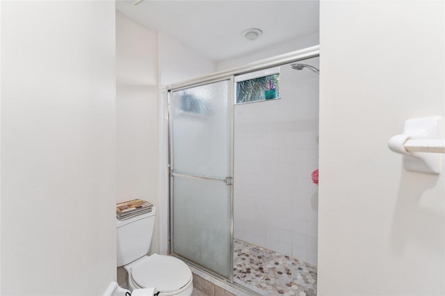 bathroom featuring a shower with door and toilet