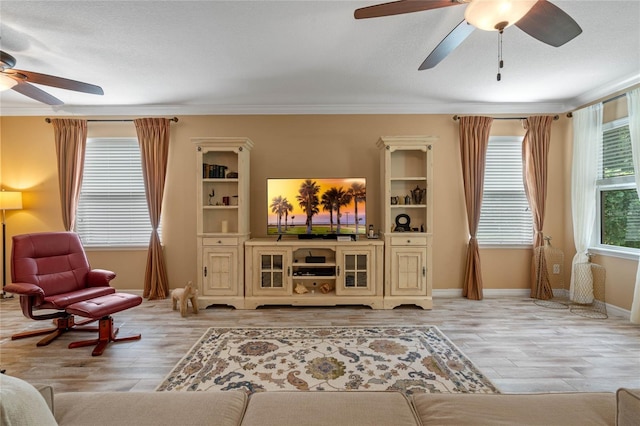 living area with light hardwood / wood-style floors, crown molding, built in shelves, and ceiling fan