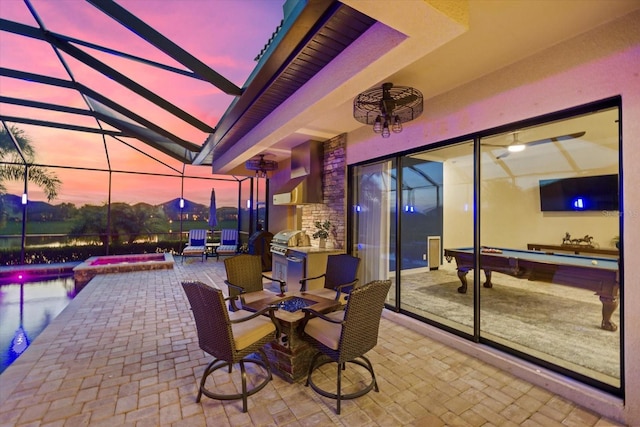 patio terrace at dusk with a lanai, ceiling fan, and grilling area