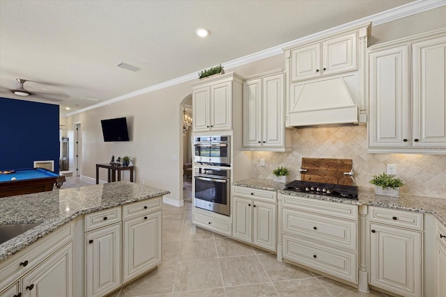 kitchen featuring billiards, black gas stovetop, premium range hood, ornamental molding, and light stone counters