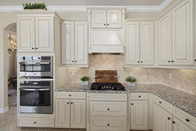 kitchen featuring tasteful backsplash, light stone countertops, stainless steel double oven, black gas cooktop, and ornamental molding