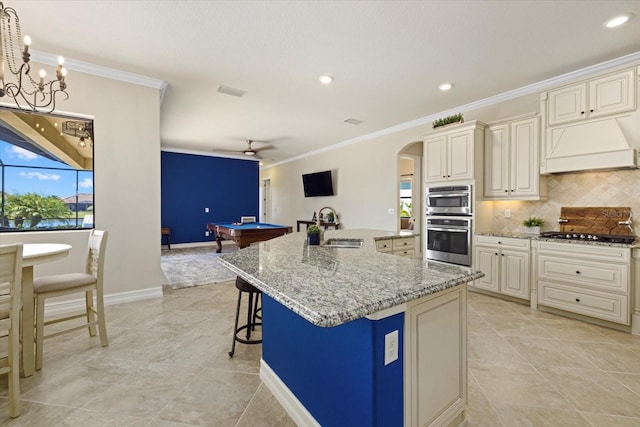 kitchen featuring cream cabinets, an island with sink, light stone countertops, decorative light fixtures, and billiards