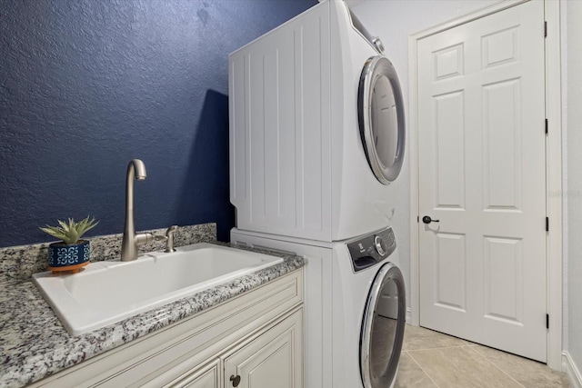 laundry area with cabinets, stacked washer and clothes dryer, sink, and light tile patterned floors