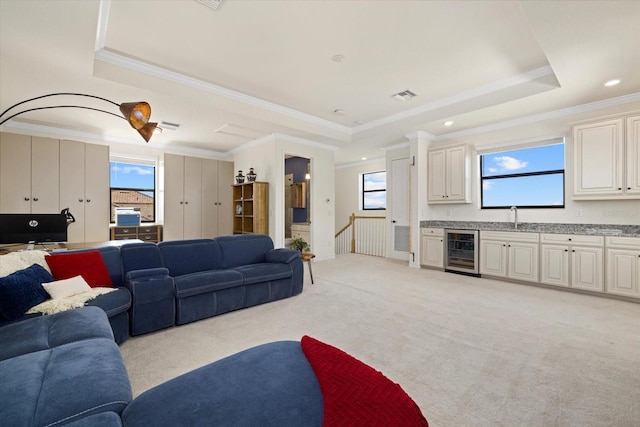 living room with wine cooler, ornamental molding, light carpet, and a raised ceiling