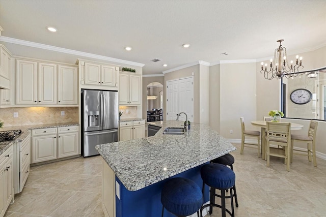 kitchen with a kitchen island with sink, cream cabinets, backsplash, sink, and appliances with stainless steel finishes