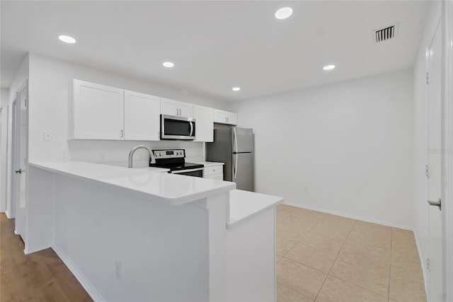 kitchen featuring appliances with stainless steel finishes, light tile patterned floors, kitchen peninsula, and white cabinets