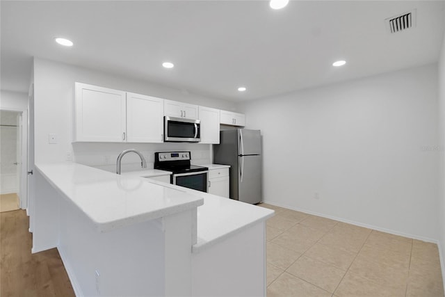 kitchen featuring stainless steel appliances, light tile patterned flooring, kitchen peninsula, and white cabinets