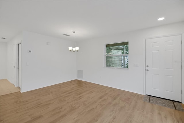 spare room with an inviting chandelier and light wood-type flooring