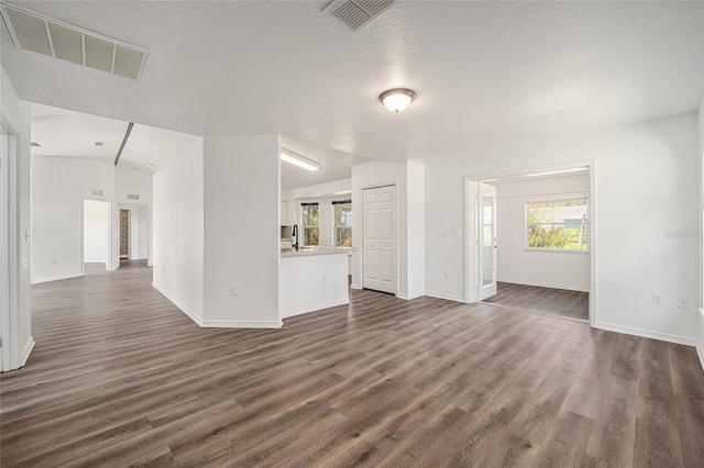 unfurnished living room with sink, a textured ceiling, lofted ceiling, and dark hardwood / wood-style flooring