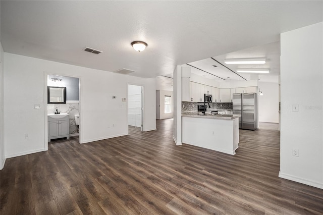 kitchen featuring kitchen peninsula, backsplash, white cabinets, appliances with stainless steel finishes, and dark hardwood / wood-style flooring