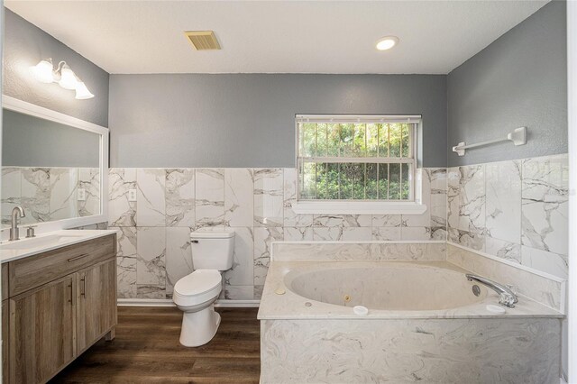 bathroom with wood-type flooring, vanity, toilet, tile walls, and a bathtub