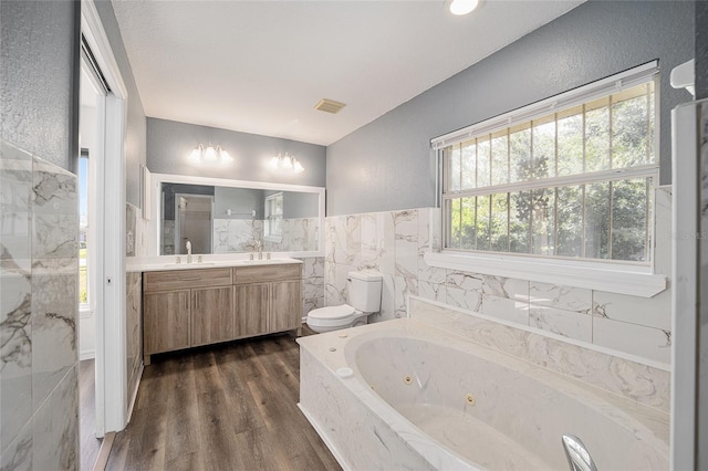 bathroom with toilet, vanity, hardwood / wood-style floors, a bathing tub, and tile walls