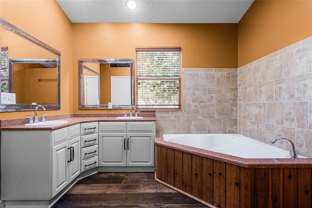 bathroom featuring tile walls, wood-type flooring, vanity, a textured ceiling, and a bathing tub