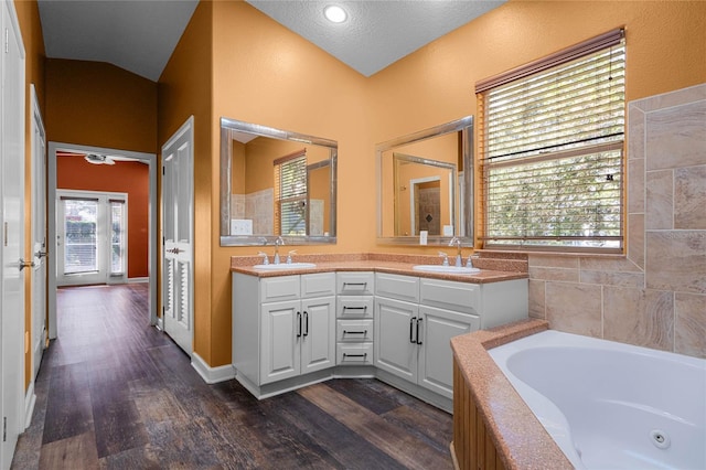 bathroom with wood-type flooring, vaulted ceiling, a textured ceiling, a bathtub, and vanity