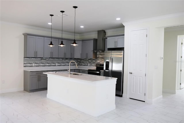 kitchen with sink, hanging light fixtures, stainless steel appliances, wall chimney exhaust hood, and a kitchen island with sink