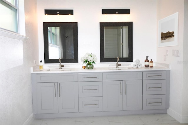 full bath featuring marble finish floor, double vanity, a sink, and baseboards