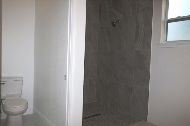 bathroom with toilet, marble finish floor, baseboards, and tiled shower