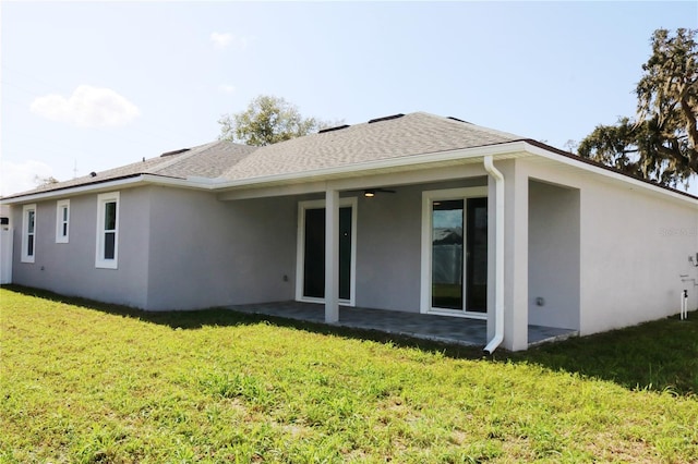 rear view of house featuring stucco siding, roof with shingles, a yard, and a patio