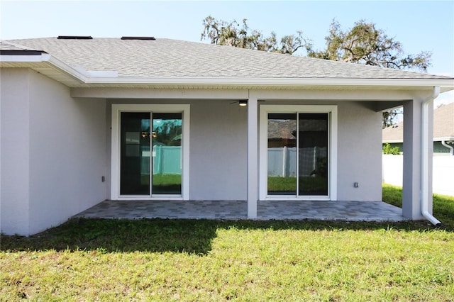 rear view of house featuring a shingled roof, a ceiling fan, a lawn, a patio area, and stucco siding