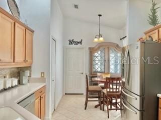 kitchen with stainless steel fridge, tasteful backsplash, light tile patterned floors, decorative light fixtures, and a high ceiling