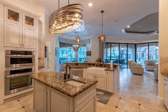 kitchen featuring sink, dark stone countertops, a kitchen island with sink, appliances with stainless steel finishes, and ornamental molding