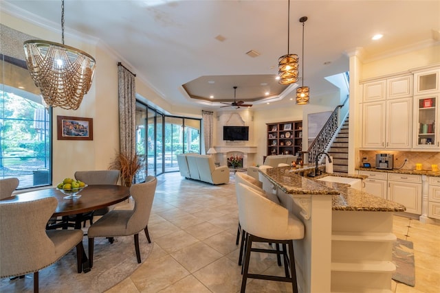 kitchen with sink, tasteful backsplash, dark stone countertops, pendant lighting, and ceiling fan with notable chandelier