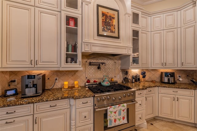 kitchen featuring light tile patterned floors, tasteful backsplash, dark stone countertops, high end stainless steel range, and white cabinets