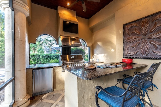 interior space featuring stainless steel refrigerator, plenty of natural light, wall chimney exhaust hood, and dark stone countertops