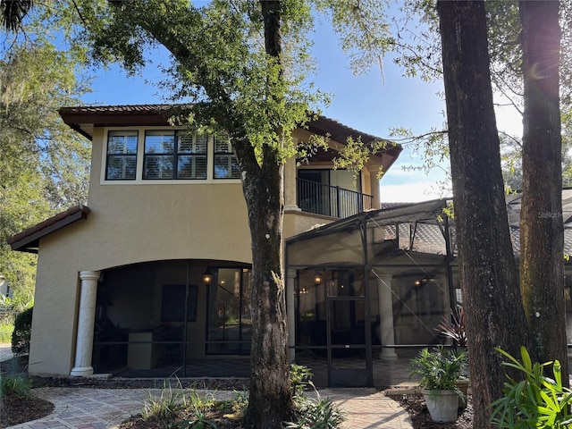 back of house with glass enclosure, a balcony, and a patio