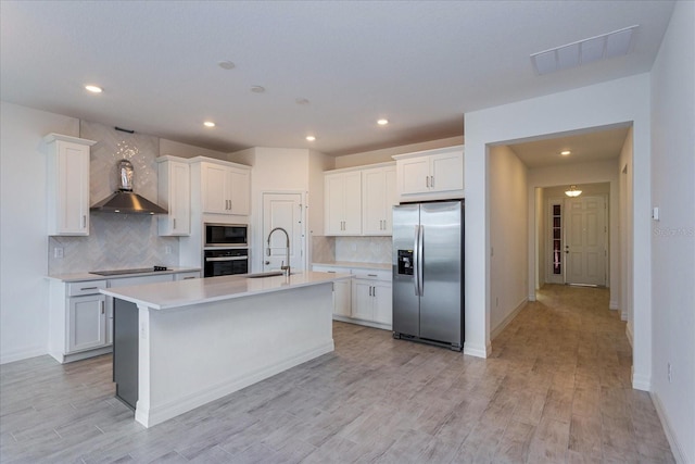 kitchen with black appliances, sink, light hardwood / wood-style floors, white cabinets, and a kitchen island with sink